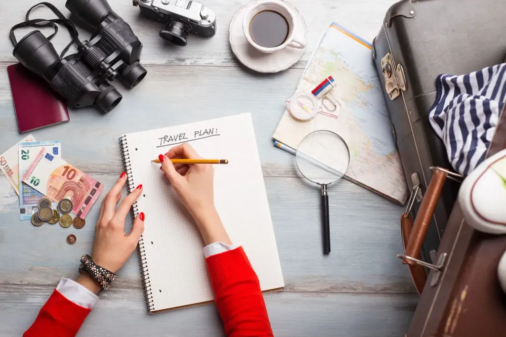 Overhead view of someone planning their trip in a notebook surrounded by travel items